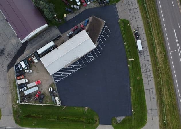Aerial view of a parking lot with vehicles next to a large building and road access.