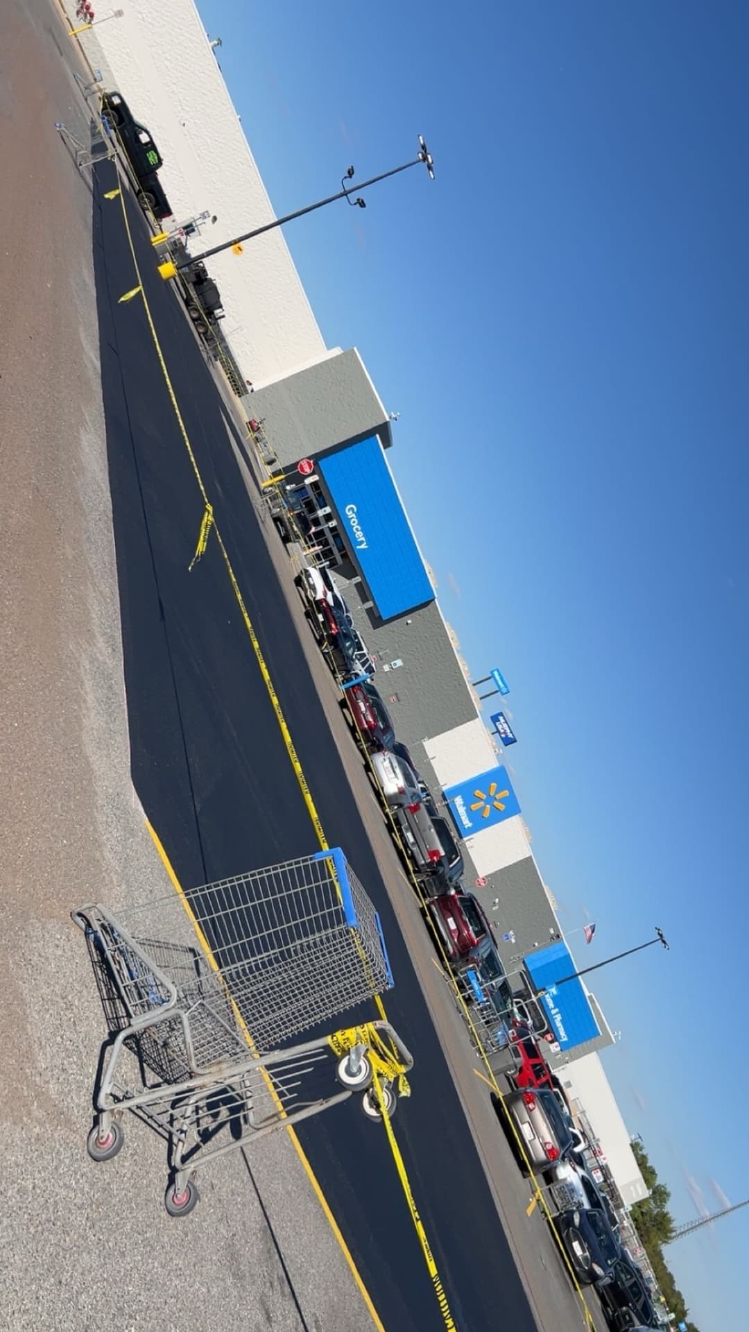 Walmart storefront with shopping cart and parked cars, surrounded by caution tape.