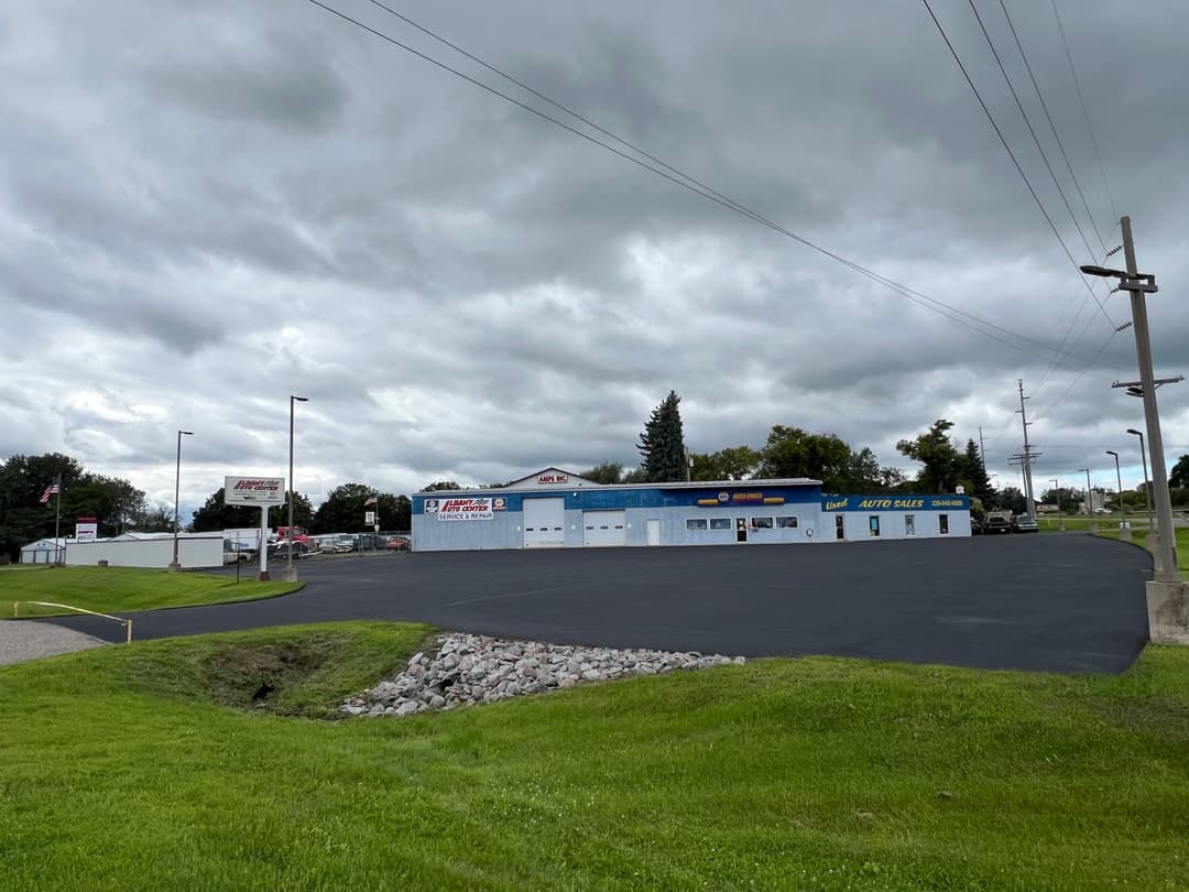 Auto repair shop on a cloudy day, featuring a large blue building and freshly paved parking lot.