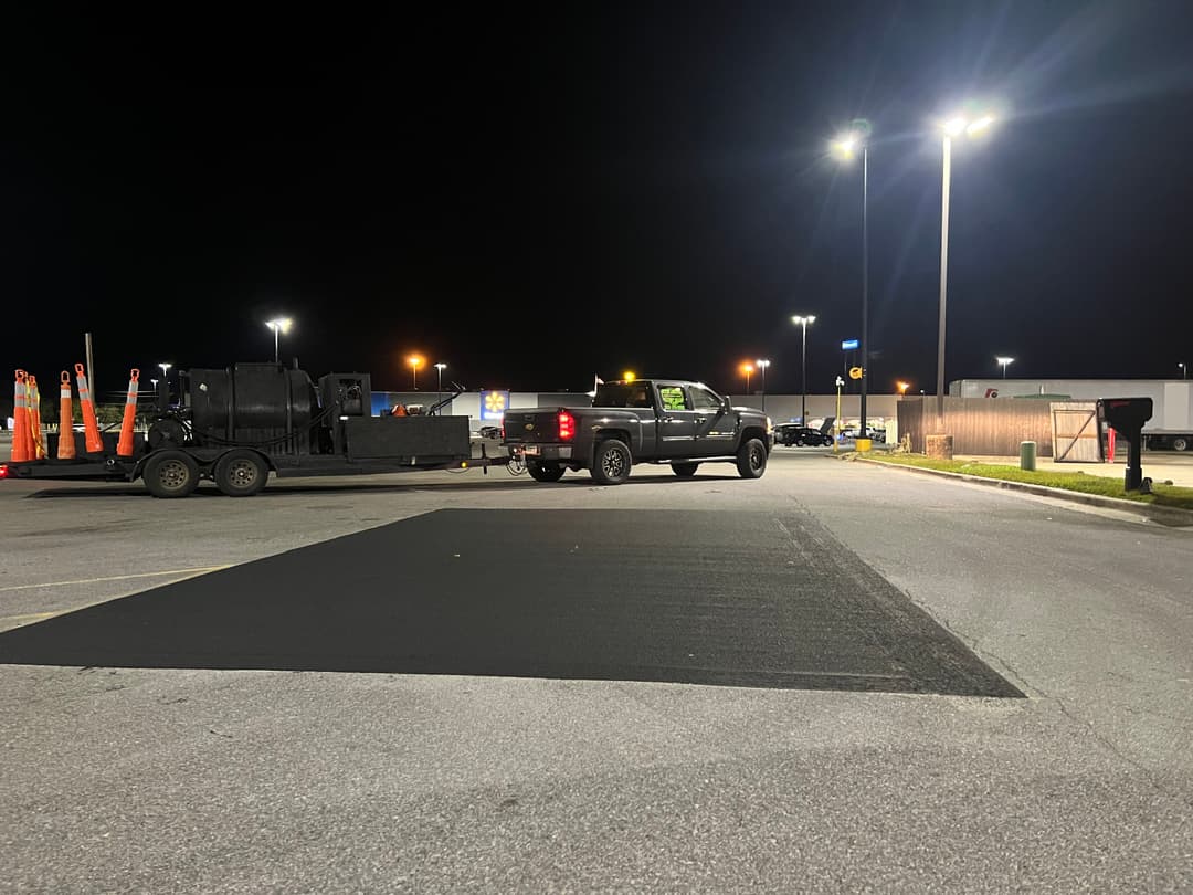 Pickup truck with trailer on a darkened parking lot, asphalt paving in progress at night.