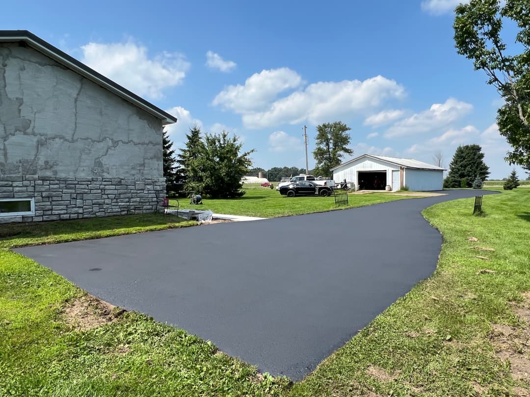 Freshly paved driveway beside a residential home and garage, with a clear blue sky.