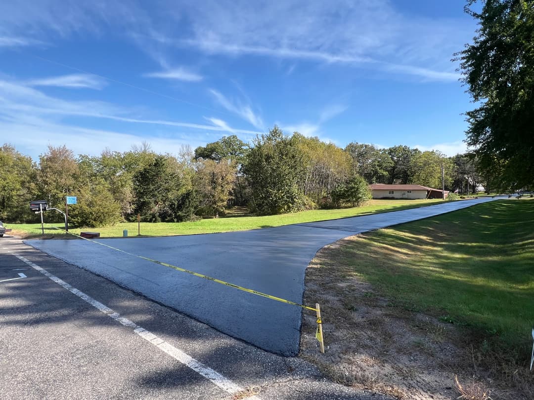 Freshly paved road intersection with clear blue sky and surrounding greenery. Caution tape visible.