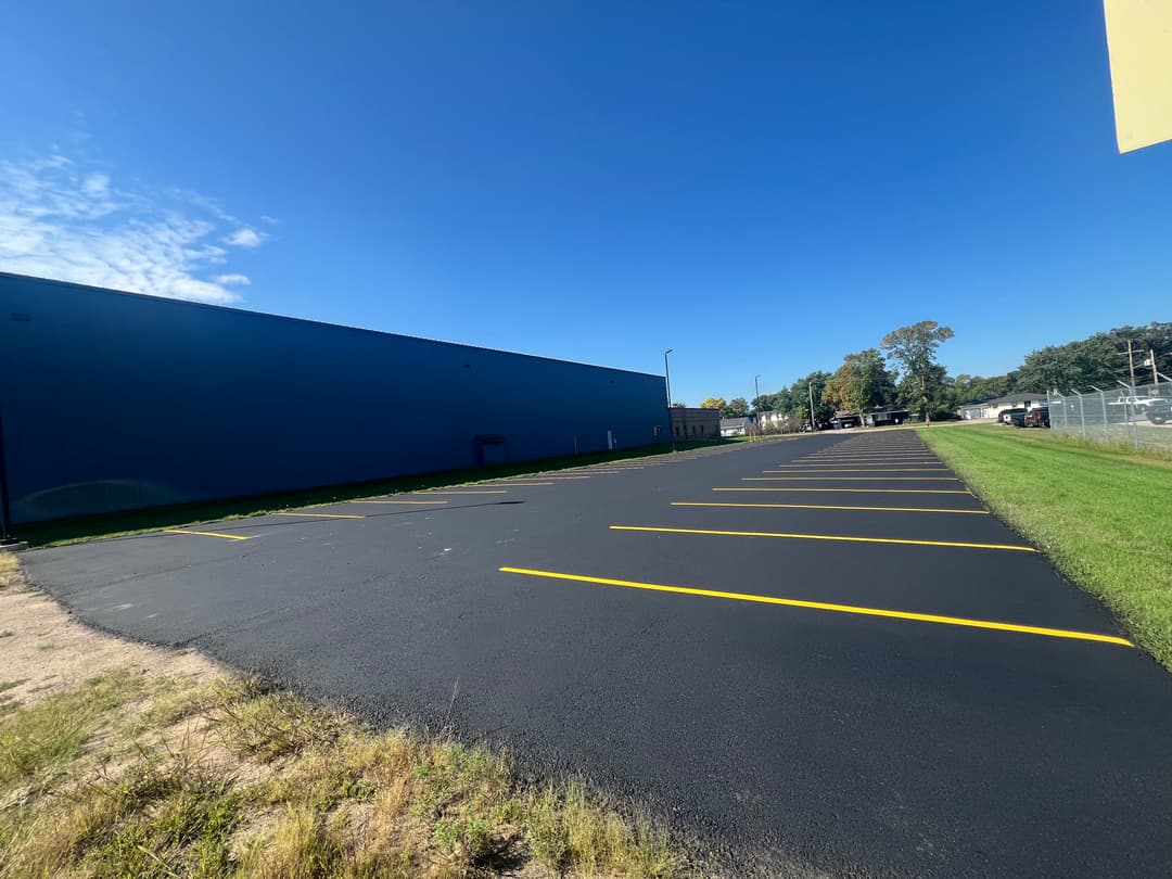 Parking lot with newly painted yellow lines beside a blue commercial building under clear sky.