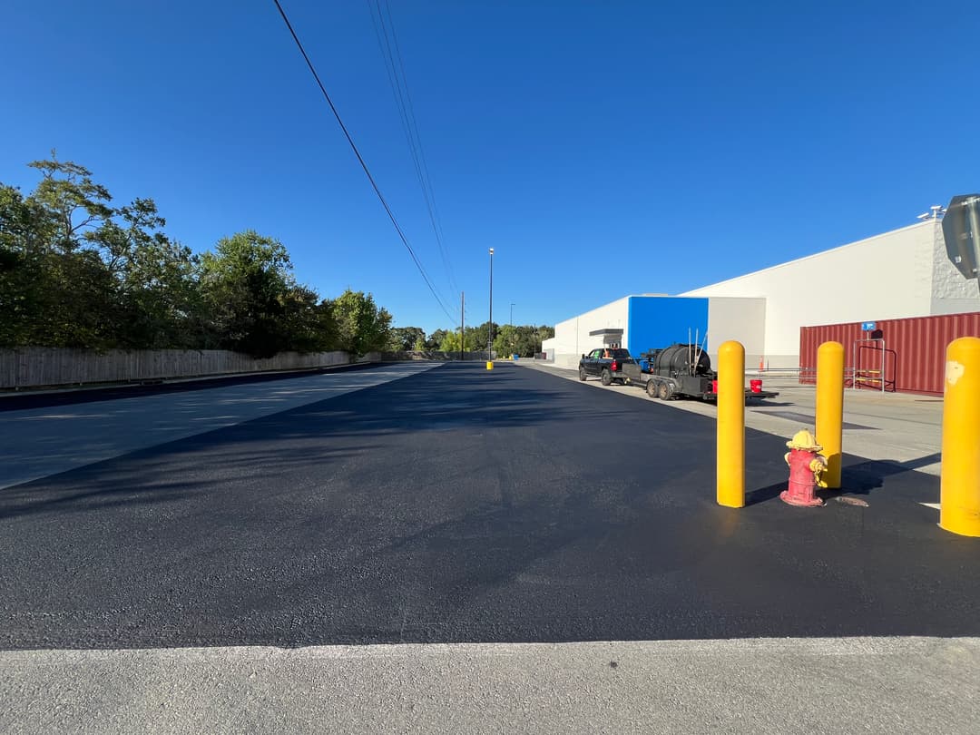 View of a newly paved parking lot with yellow bollards and a blue building in the background.