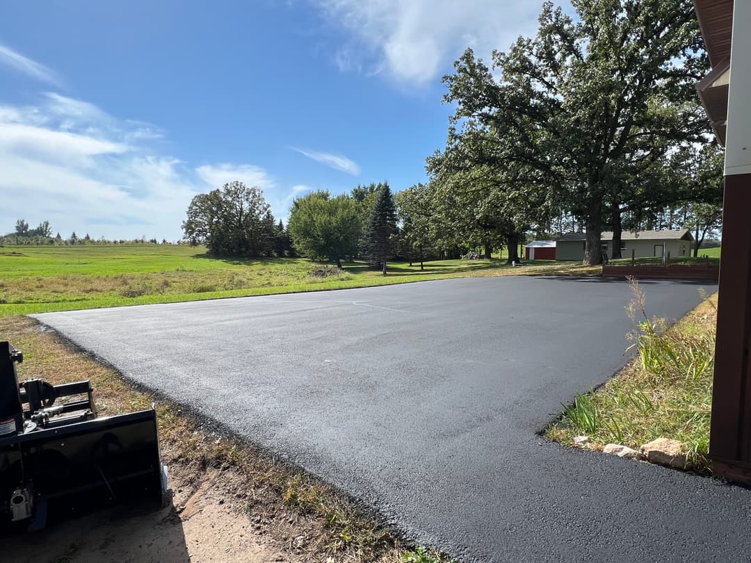 freshly paved driveway with lush green grass and trees under a blue sky