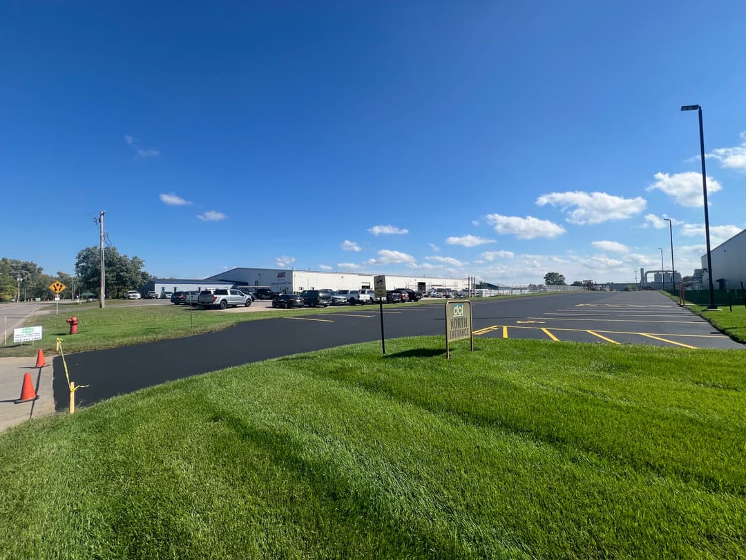 Clear view of a paved parking lot with grassy area and blue sky, indicating a commercial location.