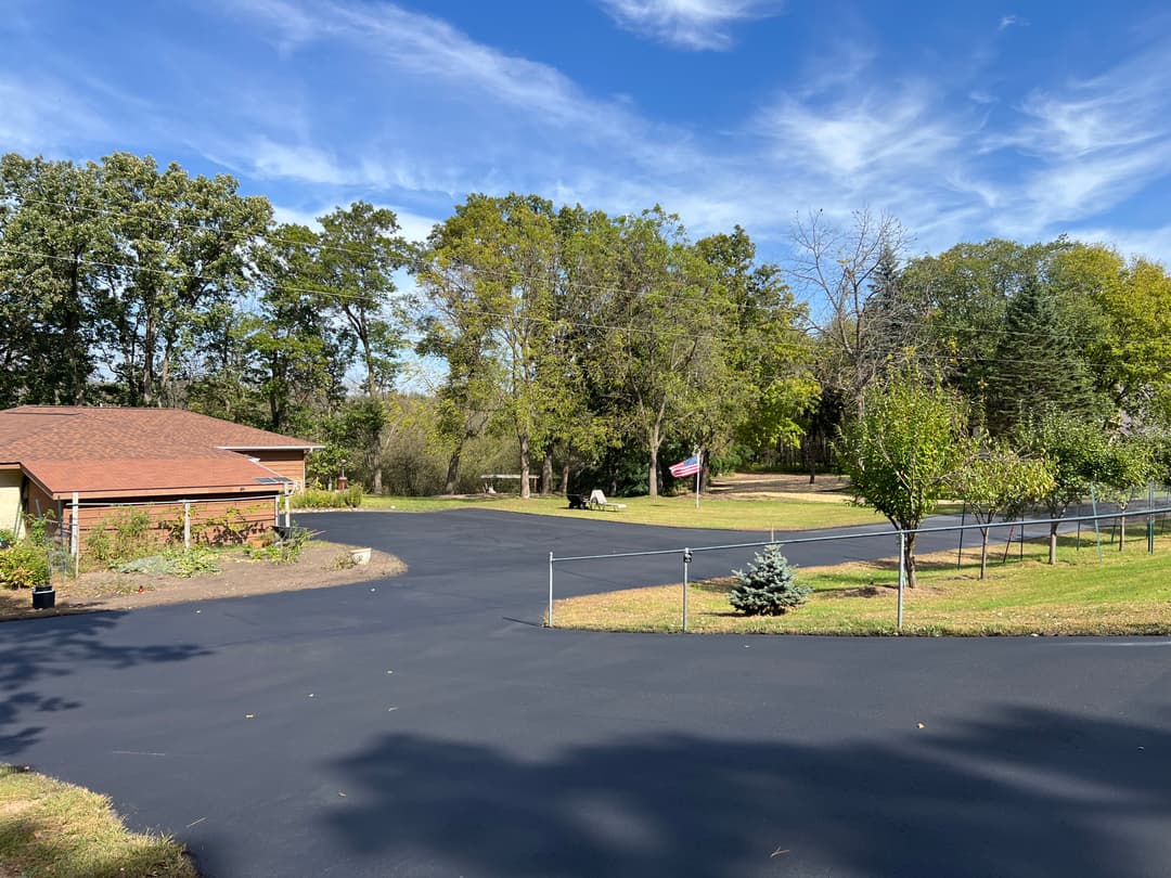 Residential area with freshly paved asphalt driveway, trees, and clear blue sky.
