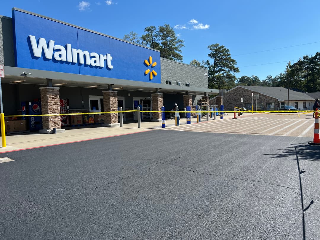 Walmart storefront with yellow caution tape and empty parking lot under clear blue sky.