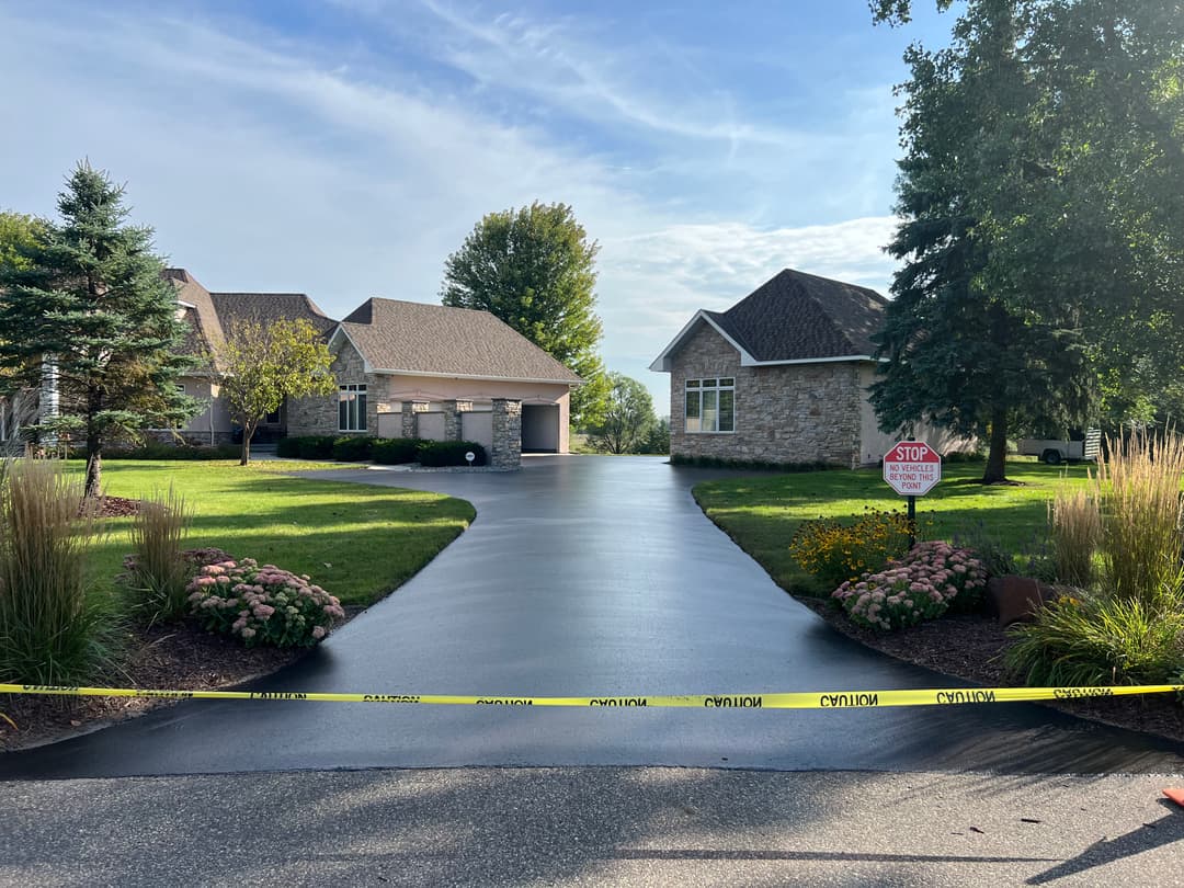Caution tape across a driveway leading to residential homes with lush landscaping.