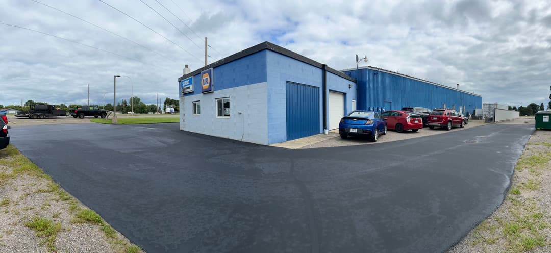 Commercial building with blue exterior, parking lot, and vehicles parked nearby on a cloudy day.