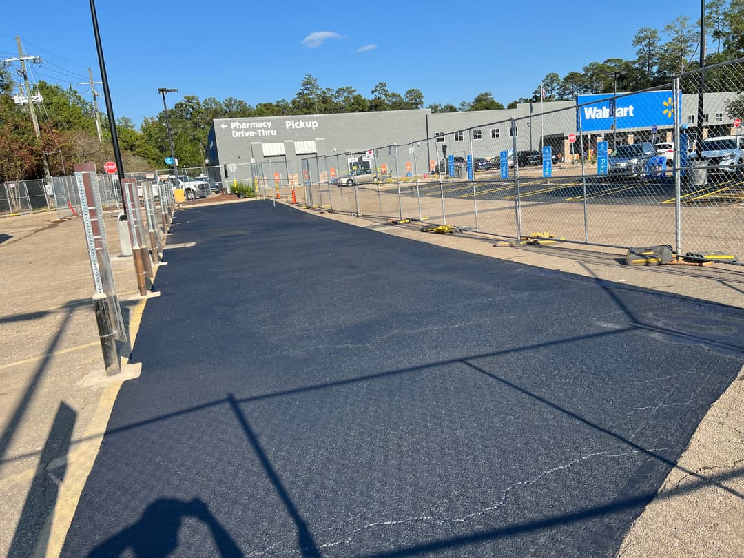 Paved pathway leading to Walmart with construction fencing and clear blue sky.