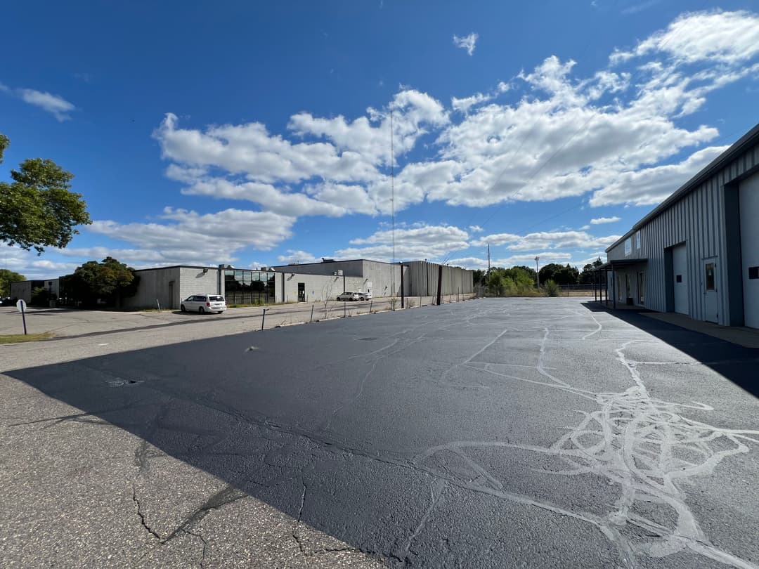 Spacious commercial lot with asphalt paving under a blue sky and scattered clouds.