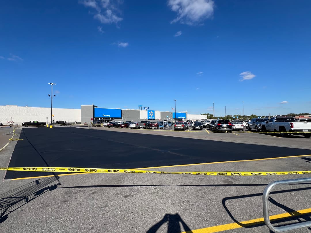 Newly paved parking lot at Walmart store with vehicles and clear blue sky.