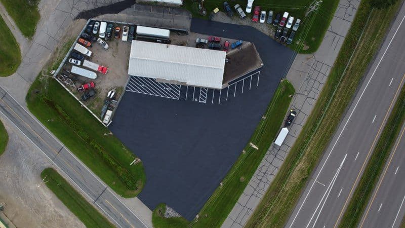Aerial view of a commercial building with parked vehicles and freshly paved lot beside a highway.