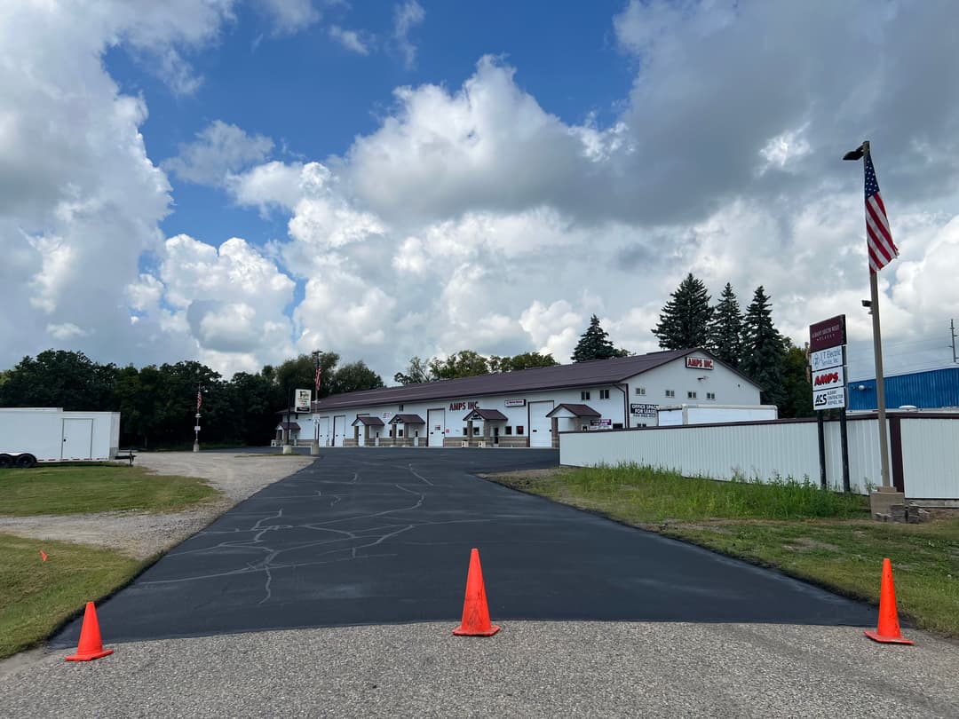 View of a commercial building with a newly paved driveway and construction cones under a cloudy sky.
