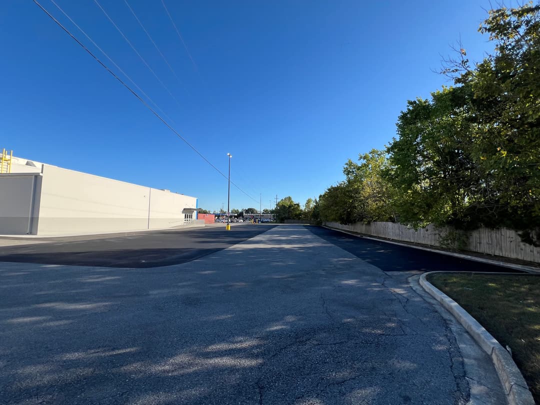 Empty parking lot under a clear blue sky with trees lining the background.