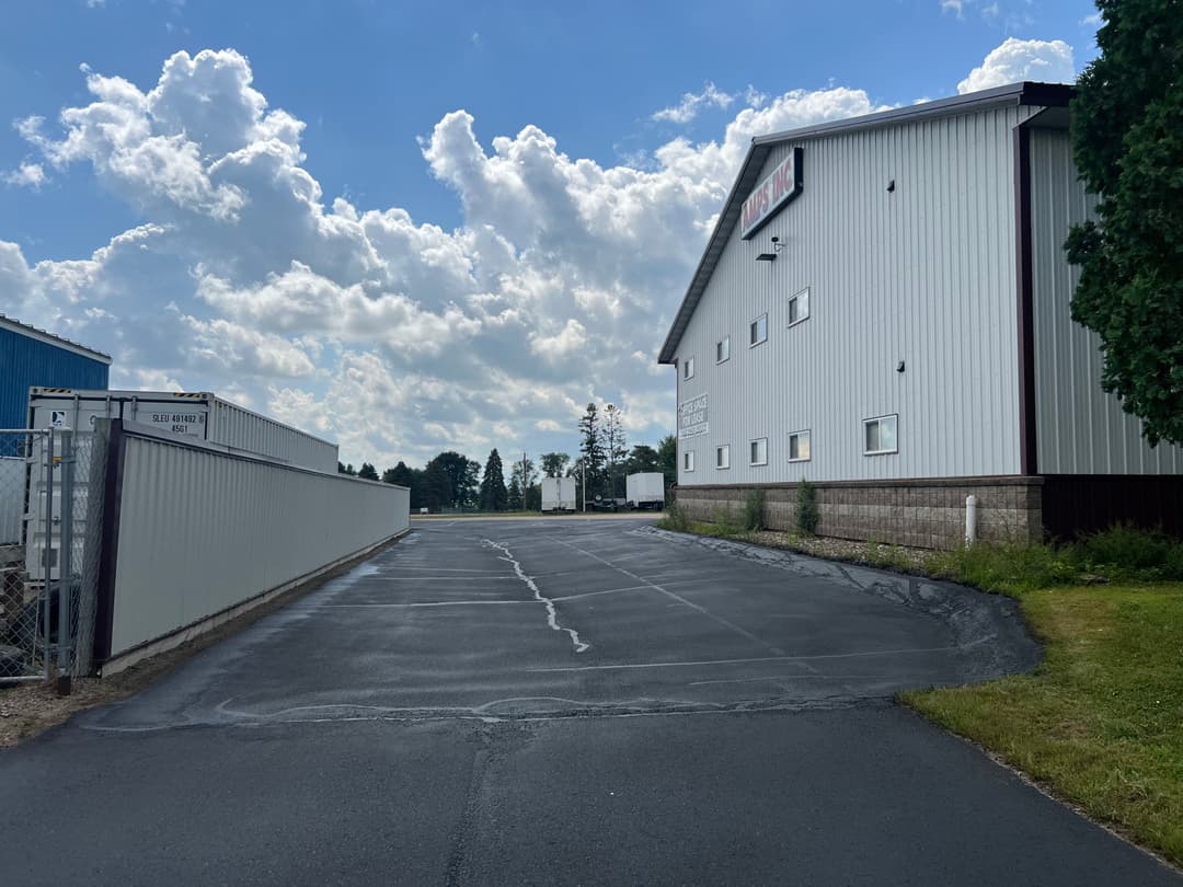 Storage facility with a large building and cloud-filled blue sky, featuring a paved driveway.