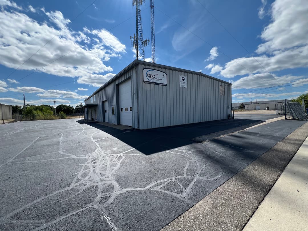 Industrial building with a sign, cell tower, and clear blue sky. Well-maintained asphalt parking lot.