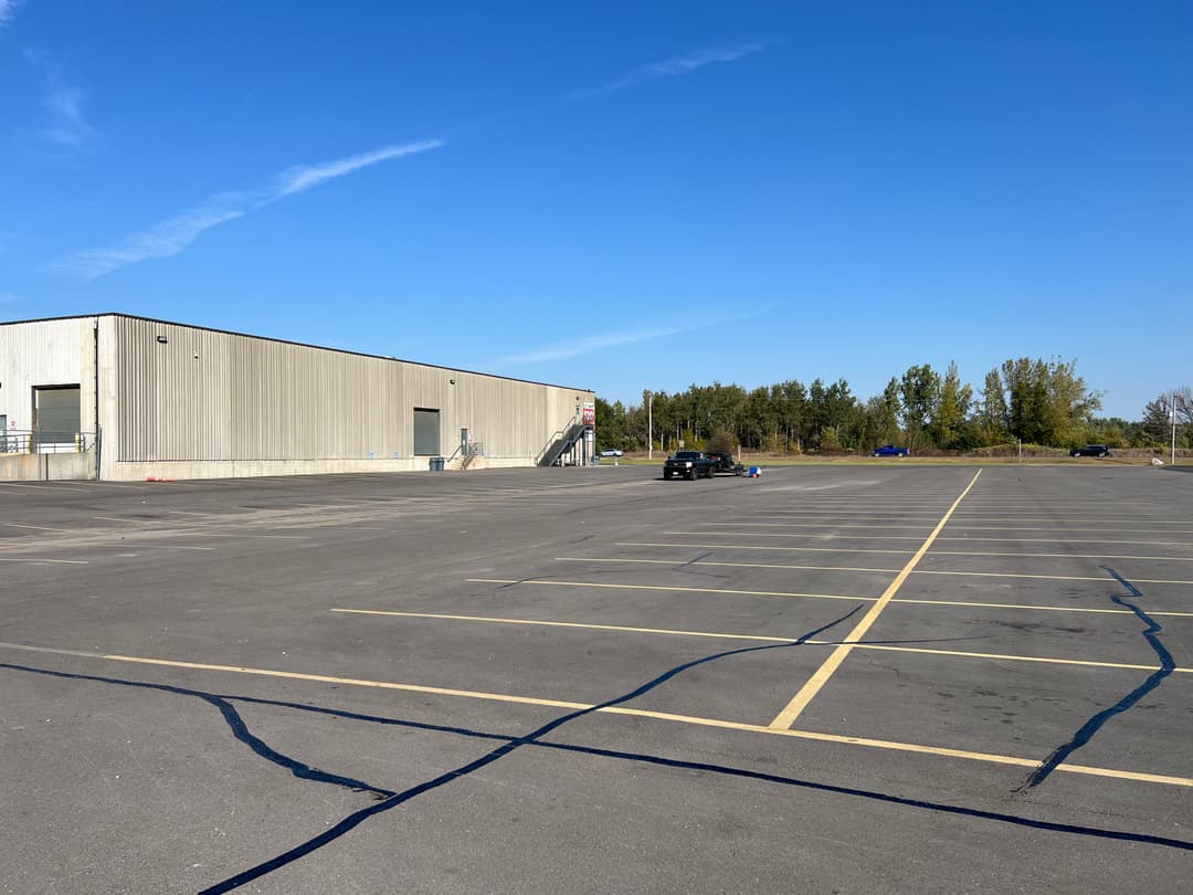 Empty parking lot beside a large industrial building under a clear blue sky.