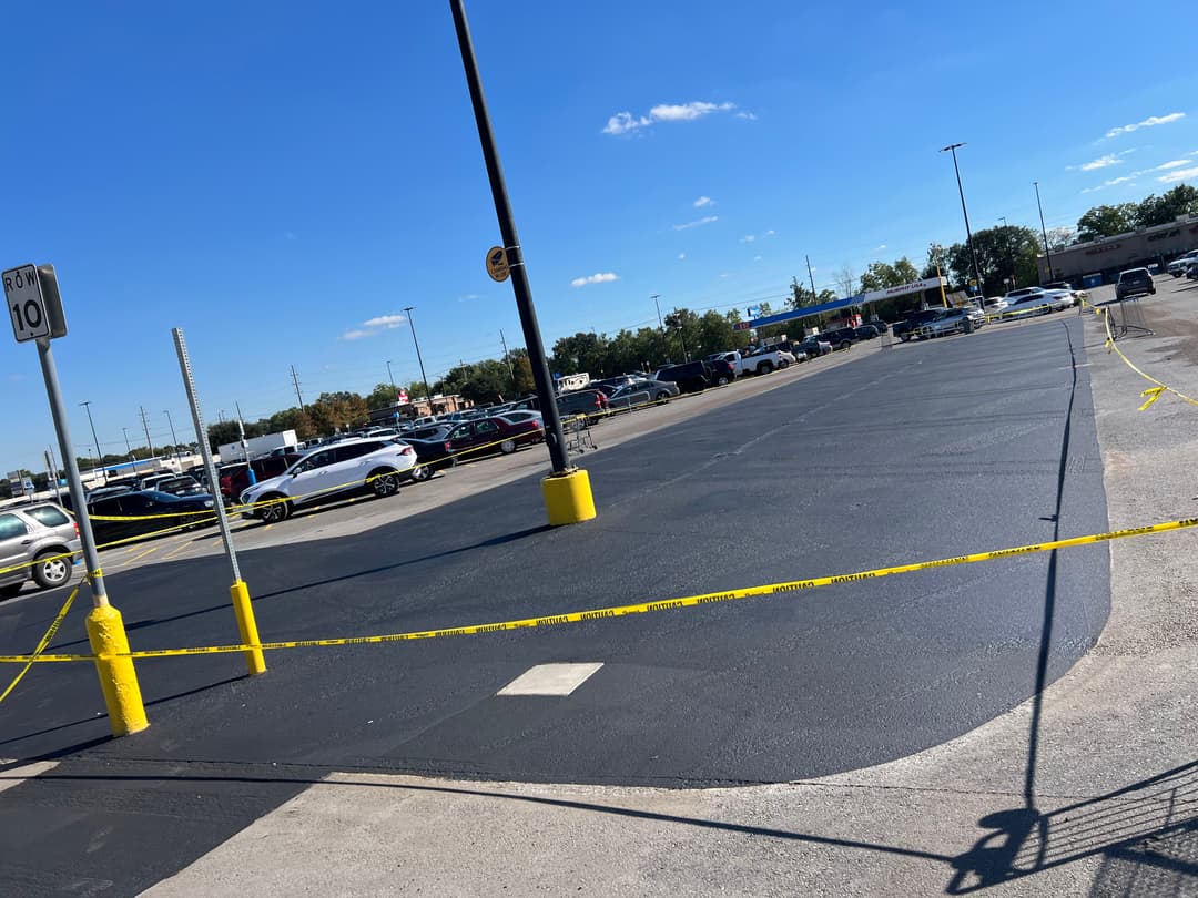 Parking lot with newly painted asphalt and yellow caution tape under clear blue sky.