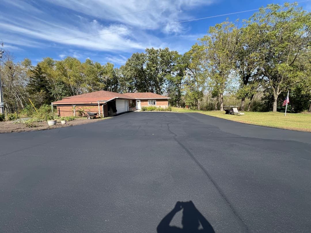 Residential home with new asphalt driveway surrounded by trees and green lawn.