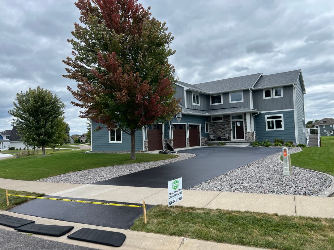 Stylish blue house with front driveway, fall-colored tree, and cloudy sky in suburban neighborhood.