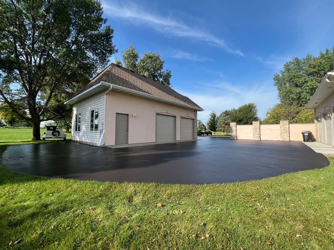 Newly paved black asphalt driveway beside a white garage under a clear blue sky.